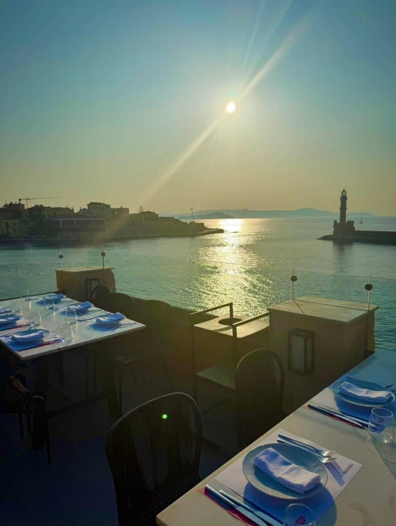 Beautiful sunset view over Chania harbour with dining tables in foreground.
